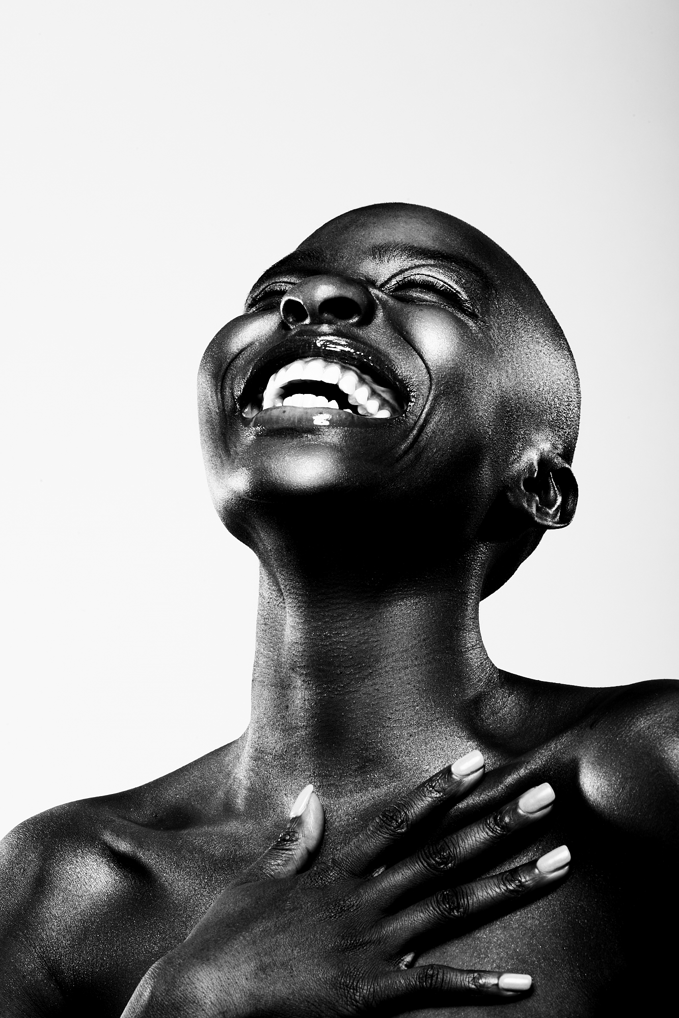 Joy: a black-and-white portrait of a person laughing with their head tilted back and a hand resting on their chest.